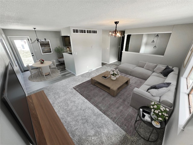 living room featuring carpet flooring, a textured ceiling, and an inviting chandelier