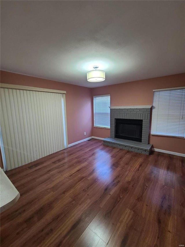 unfurnished living room featuring dark hardwood / wood-style flooring and a brick fireplace