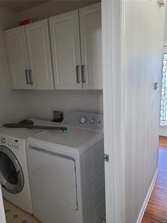 clothes washing area with washer and dryer, light hardwood / wood-style flooring, and cabinets