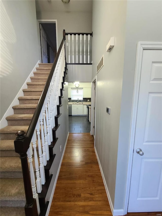 staircase featuring wood-type flooring, sink, and a towering ceiling