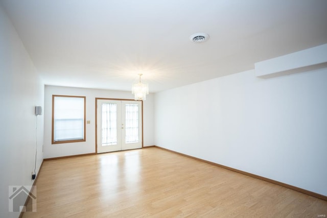 spare room featuring light wood-type flooring and a chandelier