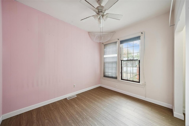 spare room with hardwood / wood-style floors, ceiling fan, and wooden walls