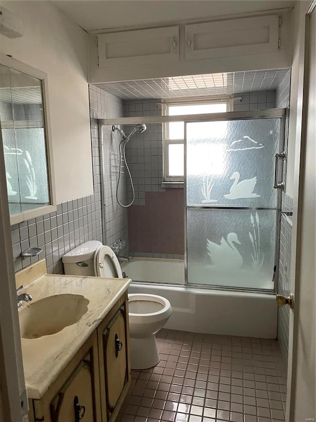 full bathroom featuring combined bath / shower with glass door, tile walls, vanity, tile patterned floors, and toilet