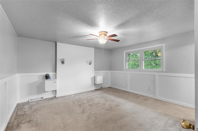 empty room with ceiling fan, light colored carpet, and a textured ceiling