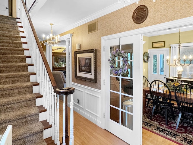 staircase featuring crown molding, an inviting chandelier, hardwood / wood-style floors, and decorative columns