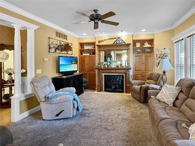 carpeted living room featuring decorative columns, crown molding, built in shelves, and ceiling fan