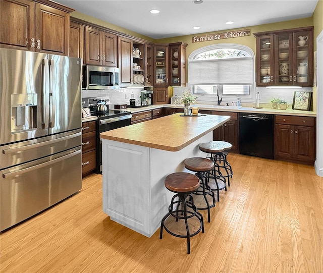 kitchen featuring light hardwood / wood-style flooring, backsplash, stainless steel appliances, a kitchen island, and a breakfast bar