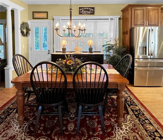 dining space with a notable chandelier, wood-type flooring, and decorative columns