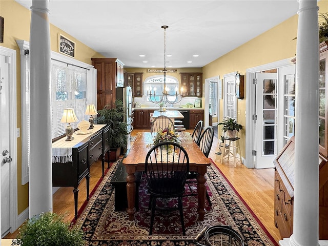 dining area featuring wood-type flooring, an inviting chandelier, and decorative columns