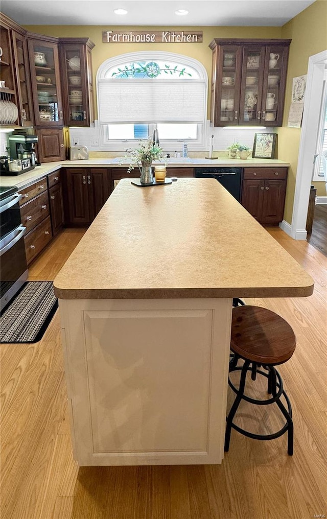 kitchen with black dishwasher, a kitchen island, a breakfast bar area, and light hardwood / wood-style floors