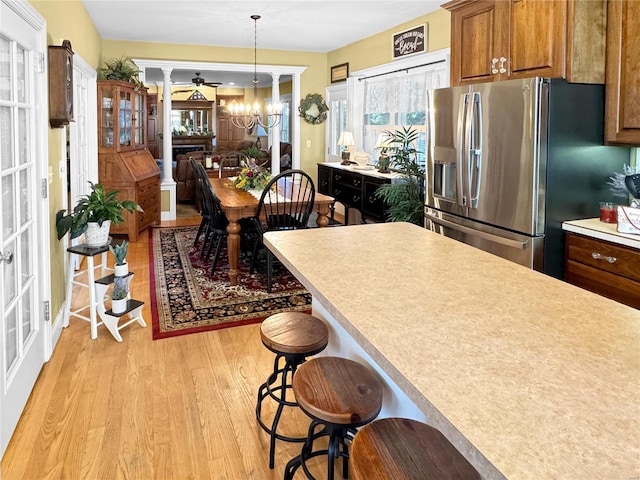 kitchen with light wood-type flooring, a notable chandelier, stainless steel fridge, a breakfast bar area, and pendant lighting