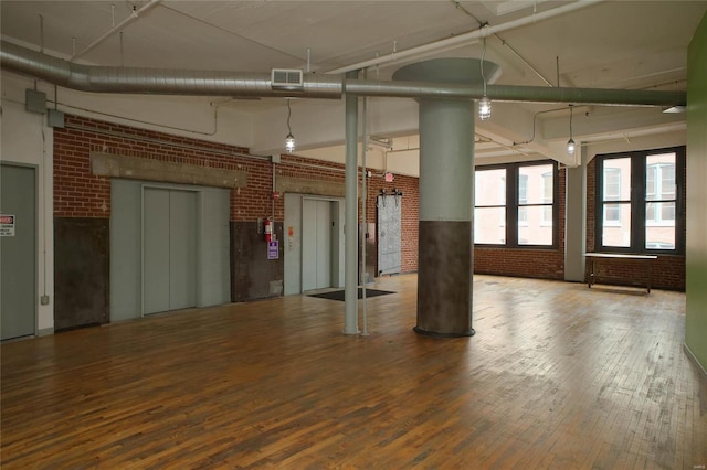 unfurnished room featuring hardwood / wood-style flooring and brick wall