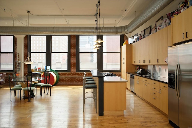 kitchen featuring brick wall, stainless steel appliances, pendant lighting, light hardwood / wood-style floors, and a kitchen island