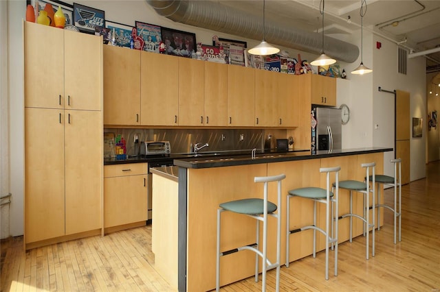 kitchen featuring light hardwood / wood-style flooring, light brown cabinetry, decorative light fixtures, a kitchen bar, and stainless steel fridge with ice dispenser