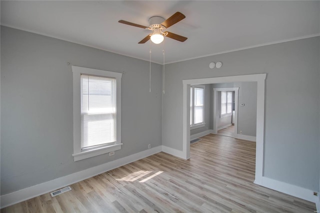 empty room with ceiling fan, a wealth of natural light, crown molding, and light hardwood / wood-style flooring