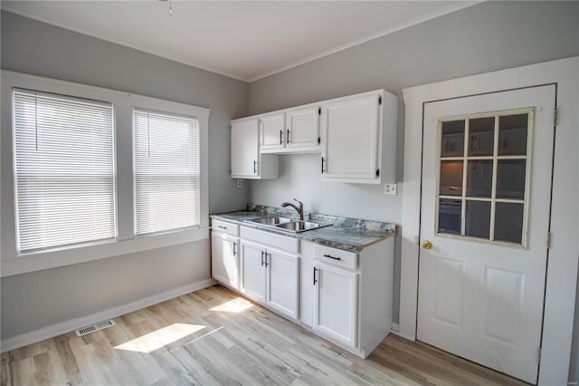 kitchen with light wood-type flooring, ornamental molding, white cabinetry, and sink