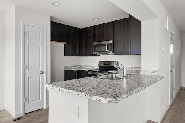 kitchen featuring dark brown cabinets, light hardwood / wood-style flooring, kitchen peninsula, sink, and appliances with stainless steel finishes