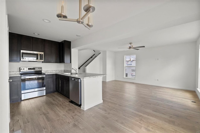 kitchen featuring ceiling fan with notable chandelier, appliances with stainless steel finishes, sink, light stone counters, and light wood-type flooring