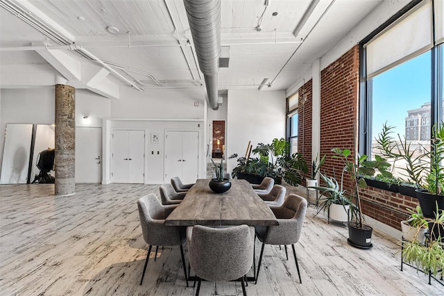 dining space featuring brick wall, wood-type flooring, ornate columns, and a towering ceiling