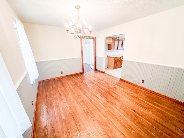 unfurnished dining area with a textured ceiling, wood walls, an inviting chandelier, and light hardwood / wood-style floors