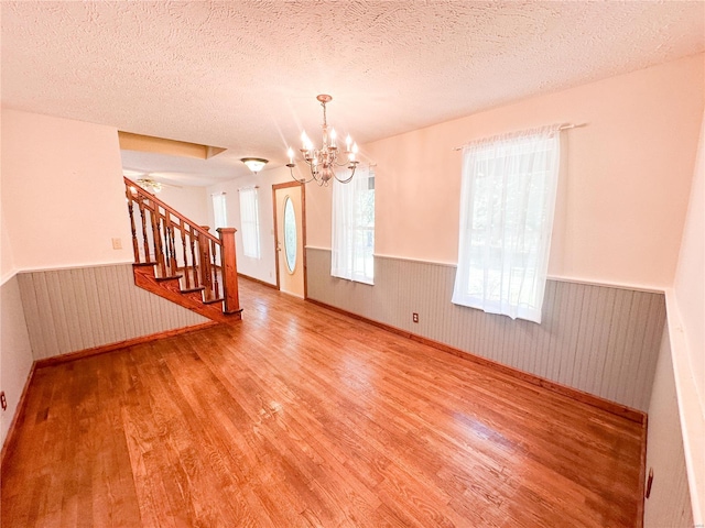 empty room featuring a chandelier, a textured ceiling, and light hardwood / wood-style flooring