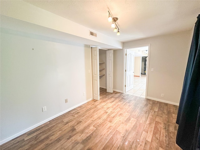 spare room featuring rail lighting, light hardwood / wood-style floors, and a textured ceiling