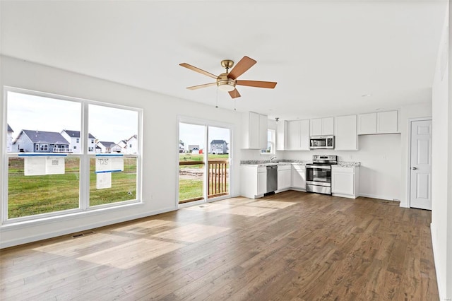 kitchen with wood finished floors, appliances with stainless steel finishes, white cabinets, baseboards, and ceiling fan