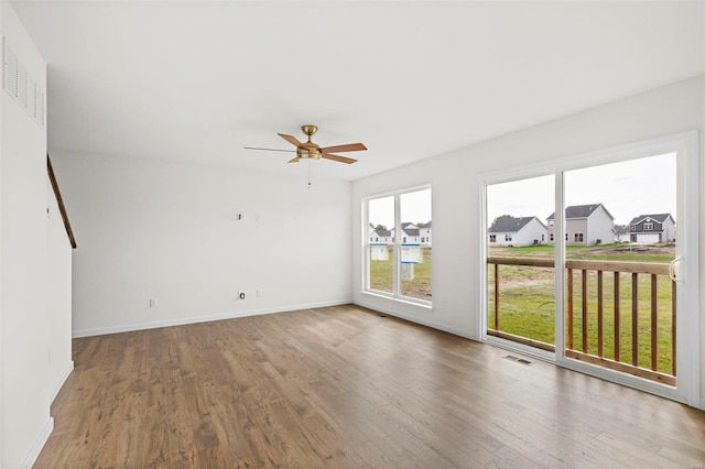 unfurnished room featuring wood finished floors, visible vents, baseboards, ceiling fan, and a residential view