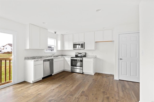 kitchen with appliances with stainless steel finishes, a wealth of natural light, hardwood / wood-style flooring, and white cabinetry