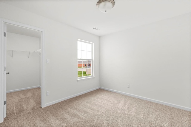 unfurnished bedroom with a walk in closet, light colored carpet, and a closet