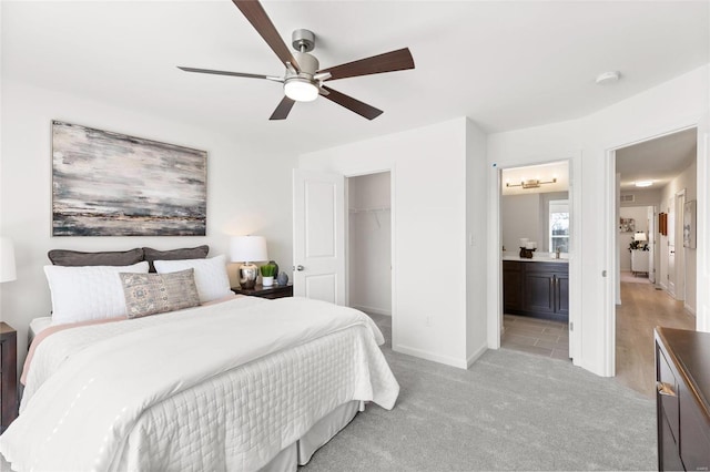 bedroom featuring a ceiling fan, baseboards, ensuite bath, a closet, and light colored carpet