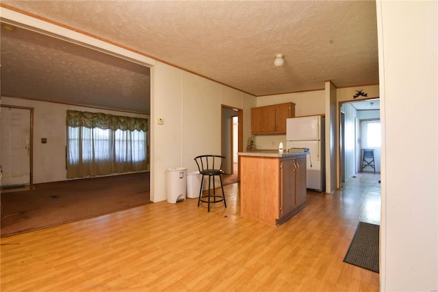 kitchen with a breakfast bar, light hardwood / wood-style floors, kitchen peninsula, white fridge, and a textured ceiling