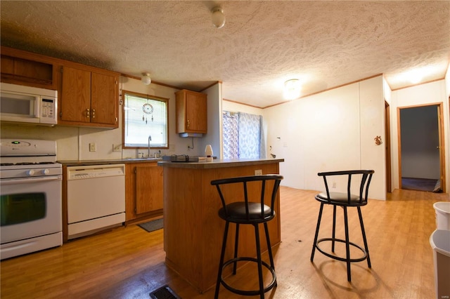 kitchen featuring light wood-type flooring, white appliances, a kitchen island, sink, and a kitchen bar