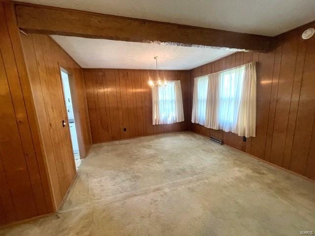 carpeted spare room featuring a notable chandelier, wood walls, and beam ceiling