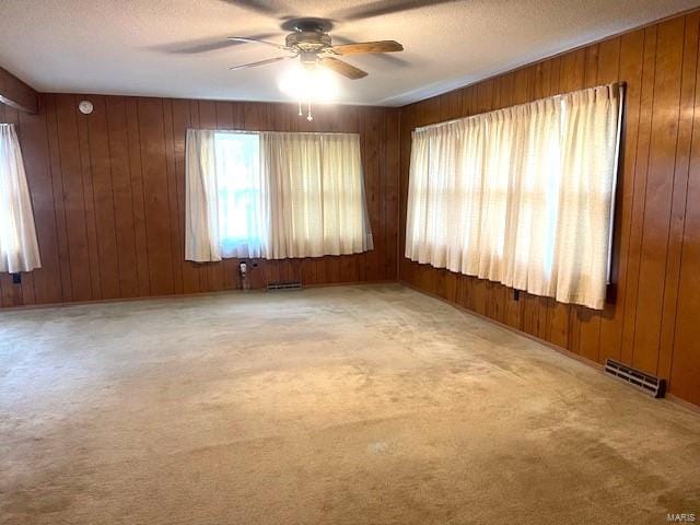 carpeted empty room with a textured ceiling, wooden walls, and ceiling fan