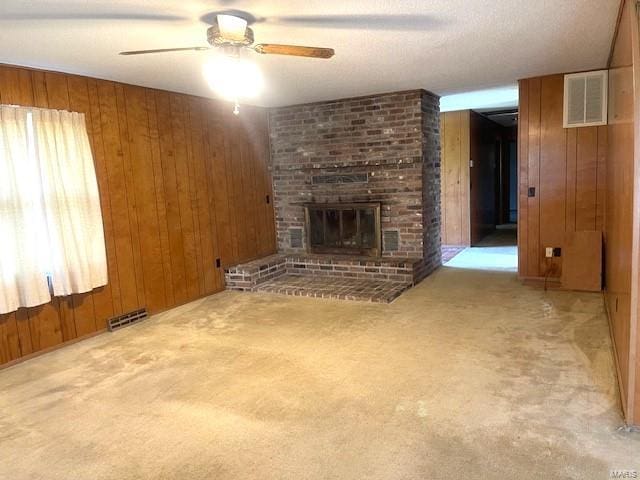 unfurnished living room with wood walls, ceiling fan, light carpet, and a brick fireplace