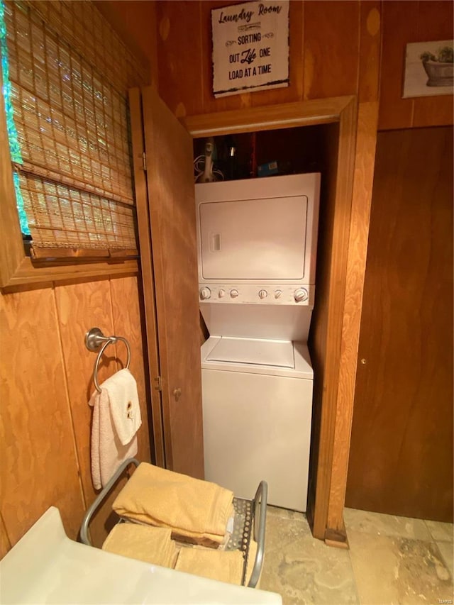 laundry room with wooden walls and stacked washer / drying machine