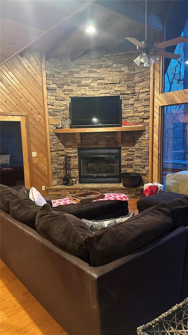 living room featuring beamed ceiling, a fireplace, ceiling fan, wood walls, and hardwood / wood-style flooring