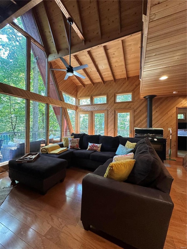 living room featuring beamed ceiling, wooden ceiling, a wood stove, high vaulted ceiling, and wood walls