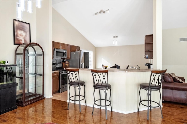 kitchen with stainless steel appliances, light hardwood / wood-style floors, a breakfast bar area, kitchen peninsula, and high vaulted ceiling