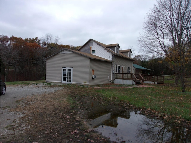 view of property exterior featuring a lawn, a wooden deck, and french doors