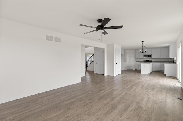 unfurnished living room with sink, ceiling fan with notable chandelier, and hardwood / wood-style flooring