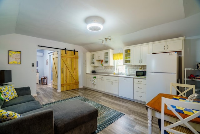 kitchen with lofted ceiling, a barn door, white appliances, and light hardwood / wood-style floors