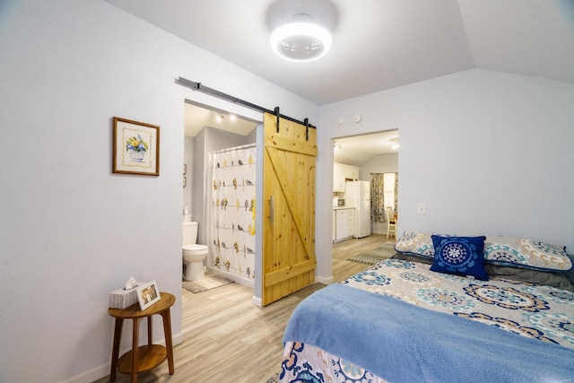 bedroom with light hardwood / wood-style floors, connected bathroom, lofted ceiling, a barn door, and white refrigerator