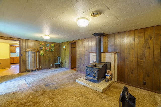 basement with a wood stove, carpet flooring, and wood walls