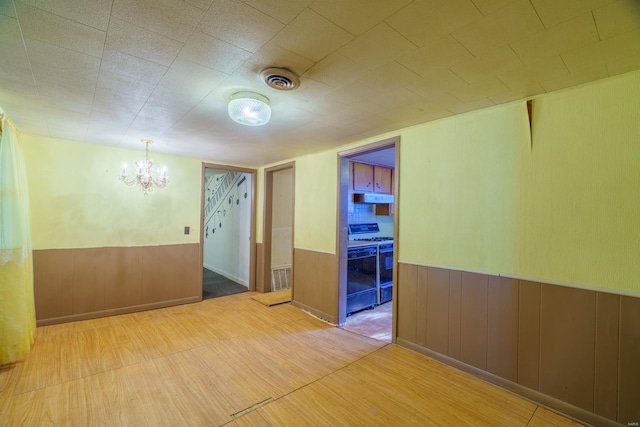 spare room with light wood-type flooring, an inviting chandelier, and wooden walls