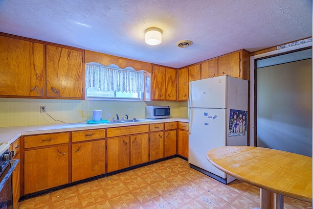 kitchen with appliances with stainless steel finishes, a textured ceiling, sink, and decorative backsplash