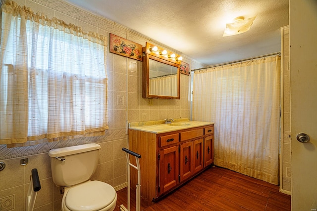 bathroom featuring toilet, vanity, a textured ceiling, tile walls, and hardwood / wood-style flooring