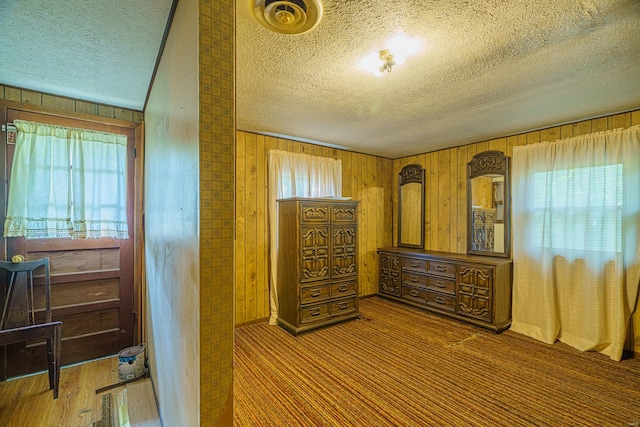 bedroom featuring multiple windows, wood walls, and a textured ceiling