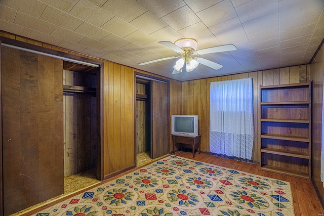 unfurnished bedroom with ceiling fan, multiple closets, wooden walls, and hardwood / wood-style flooring